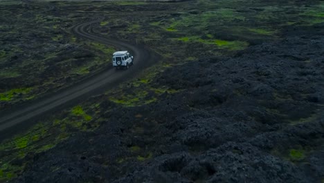aerial drone footage of a white 4x4 jeep or a truck driving through and on muddy roads with turns in iceland or greenland during a wet and damp evening or dusk weather in the mountains with snow, ice.