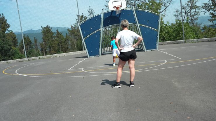 Donna e ragazzo giocano a basket in un campo all'aperto