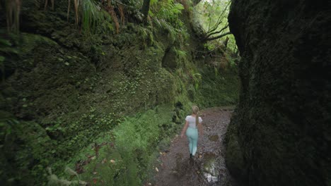 woman walking through moss covered rock wall canyon in primeval forest