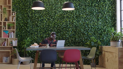 young black businessman using laptop student brainstorming working on project listening to music in trendy office workplace