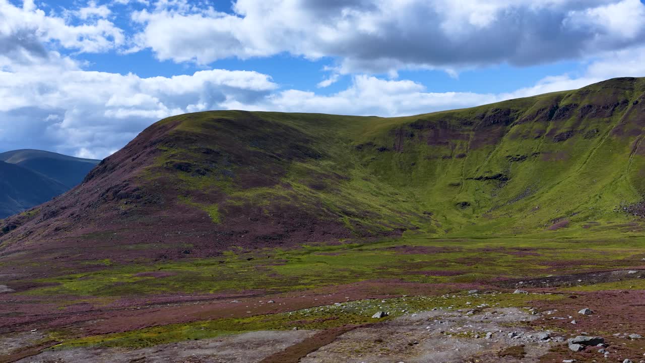 Wide daylight pan reveals green hills, rugged terrain, and dramatic clouds in Scottish Highlands