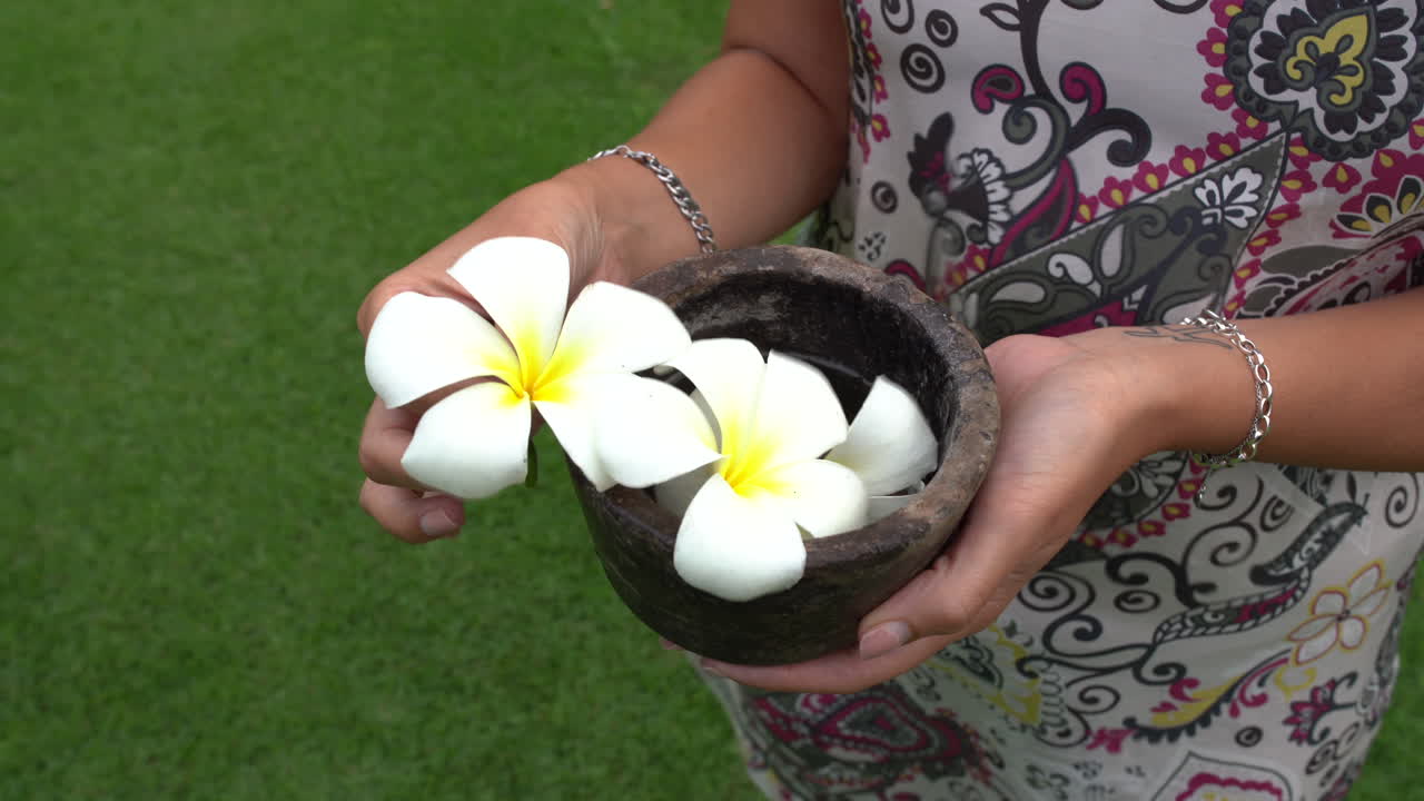 Una donna in piedi sull'erba mostra Plumeria hawaiana bianca tra le mani