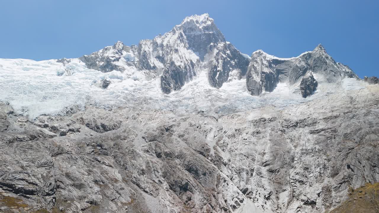 Spectacular aerial tilt up shot from a turquoise glacial lagoon to the dramatic snow-capped Taulliraju mountain peaks along the iconic Santa Cruz trek in Peru’s Cordillera Blanca