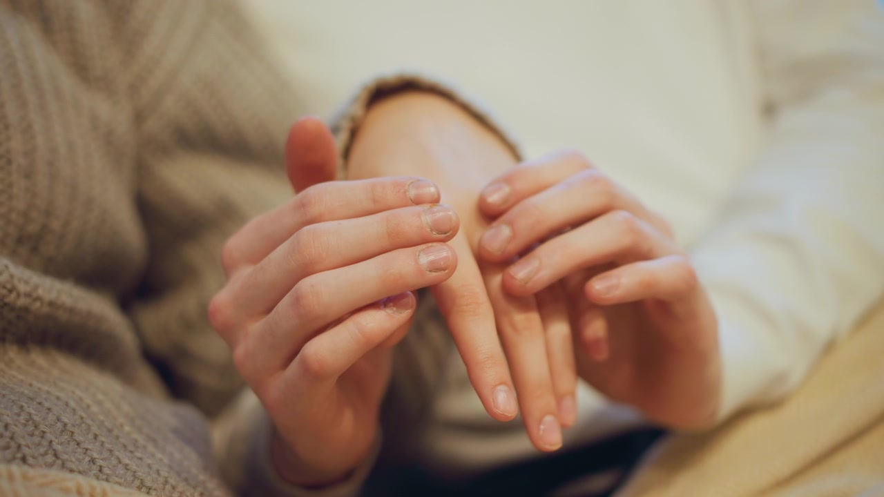 Close up of young woman gently massaging another woman hand focusing on fingers and nails. hands are positioned centrally with soft lighting highlighting skin texture details against neutral