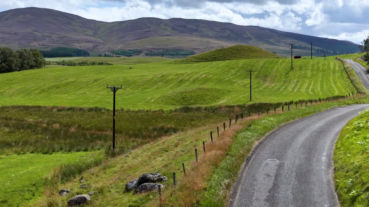 Vehicle travels winding countryside road through green meadows, rolling hills, and open rural landscape