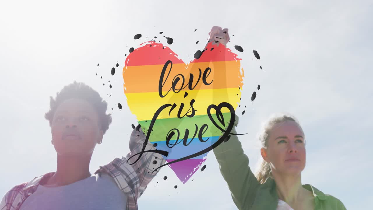 Animation of rainbow heart and love is love over lesbian couple holding hands outdoors