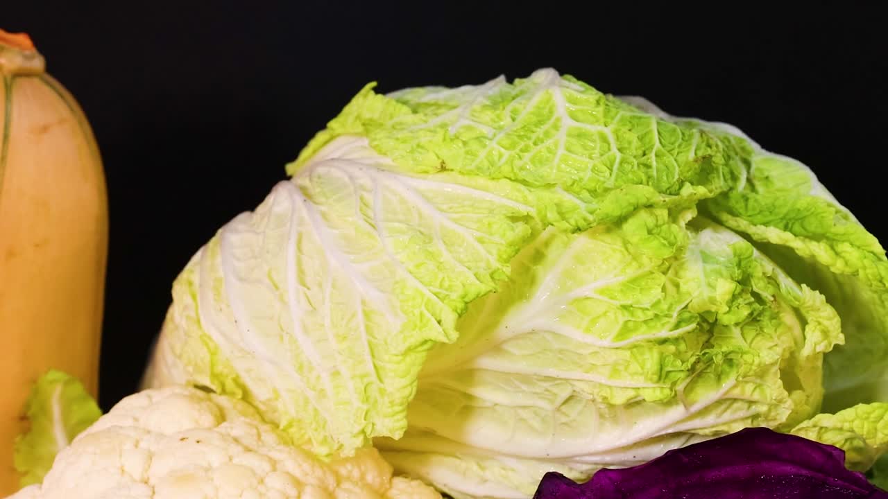 A colorful assortment of cauliflower, cabbage, zucchini, and peppers on a dark background.