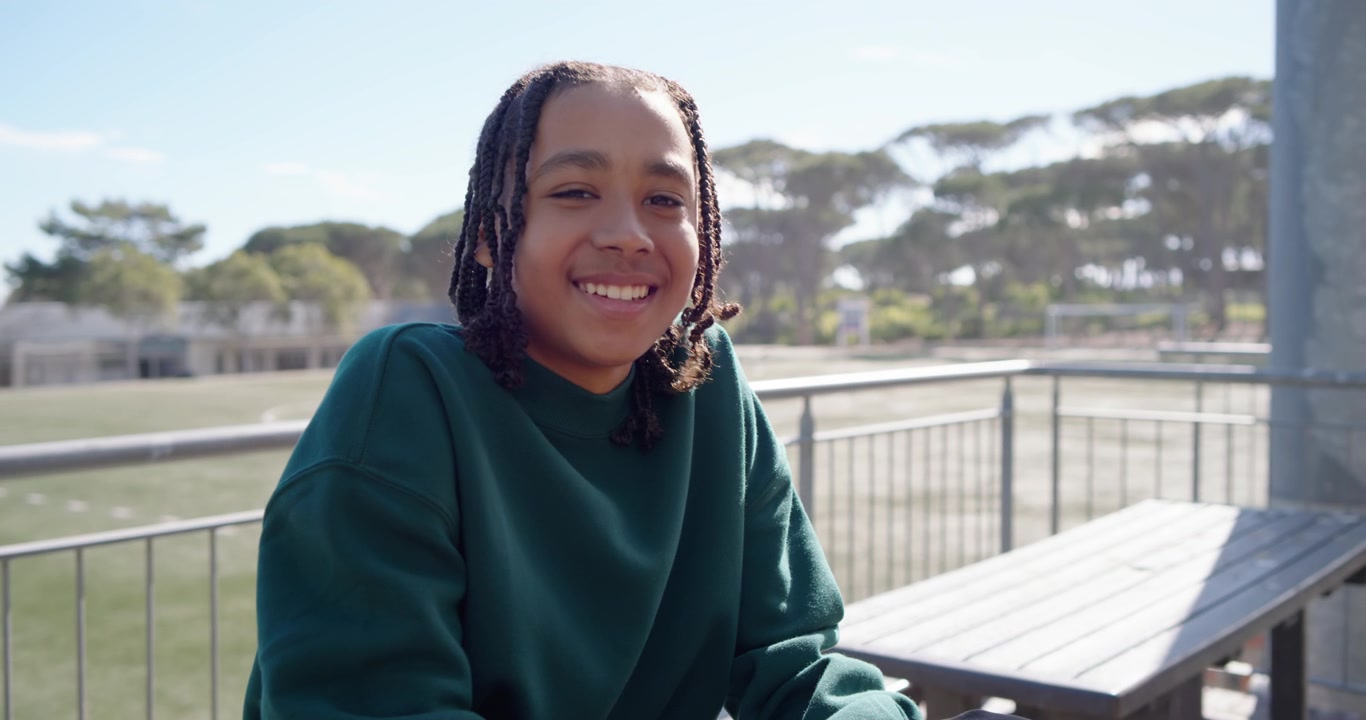 Afroamerikansk tenåring sitter på tribunen ved gressbanen, kameraet kommer nærmere og får henne til å snu hodet og smile.