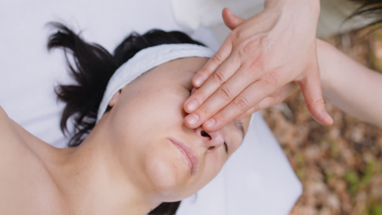 치료사 여성 의사는 숲에서 야외에서 손으로 스파 얼굴 마사지를하는 여성을 편안하게 만니다.