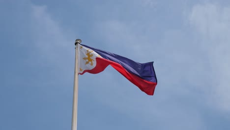 Philippine-National-Flag,-flying-to-the-right-with-some-thin-clouds-and-a-lovely-blue-sky