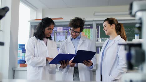 International-Group-of-Scientists-in-Laboratory.science-research,-work-and-people-concept-international-group-of-happy-scientists-with-clipboards-discussing-report-in-laboratory