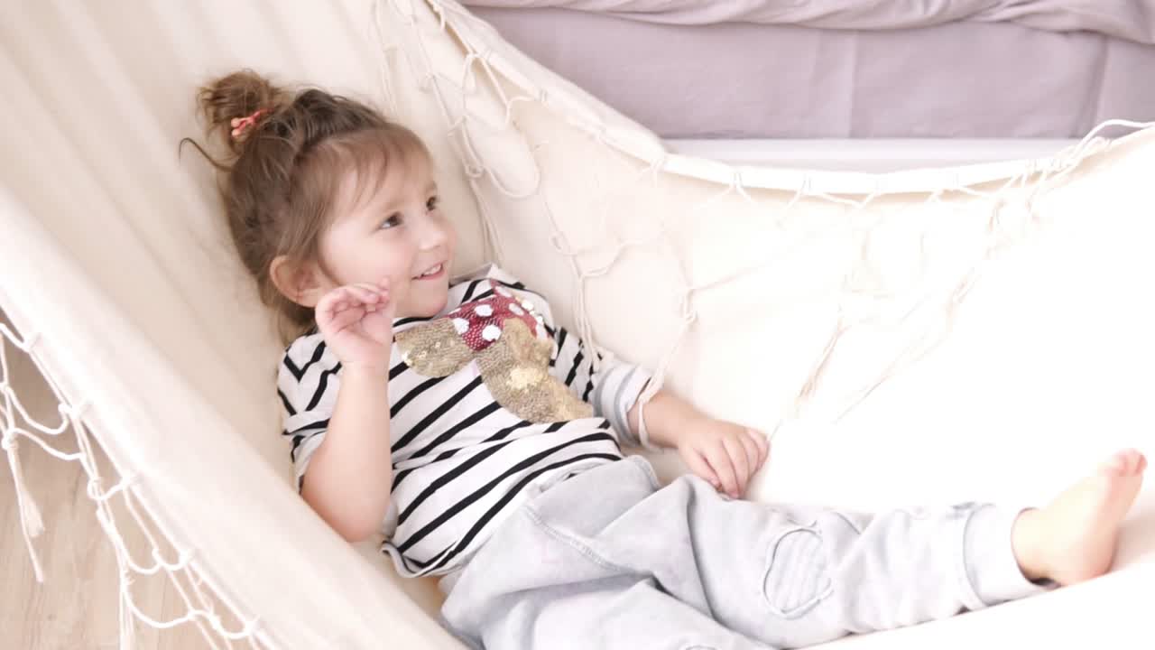 Kleines lächelndes Mädchen entspannt und schaukelt in einer weißen Hängematte. Innenaufnahme.