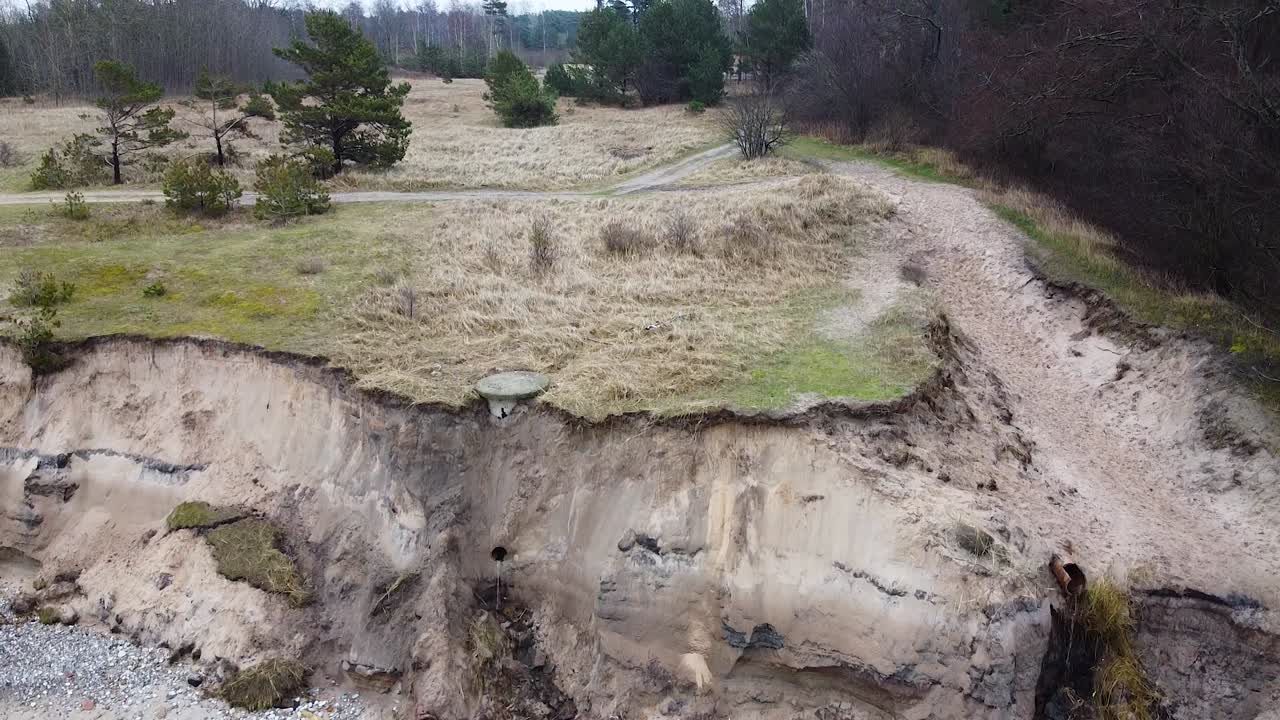 Aerial view of Baltic sea coast in overcast spring day, steep seashore dunes damaged by waves, coastal erosion, climate changes, low angle revealing drone shot moving up, ascending