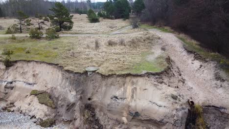 aerial view of baltic sea coast in overcast spring day, steep seashore dunes damaged by waves, coastal erosion, climate changes, low angle revealing drone shot moving up, ascending