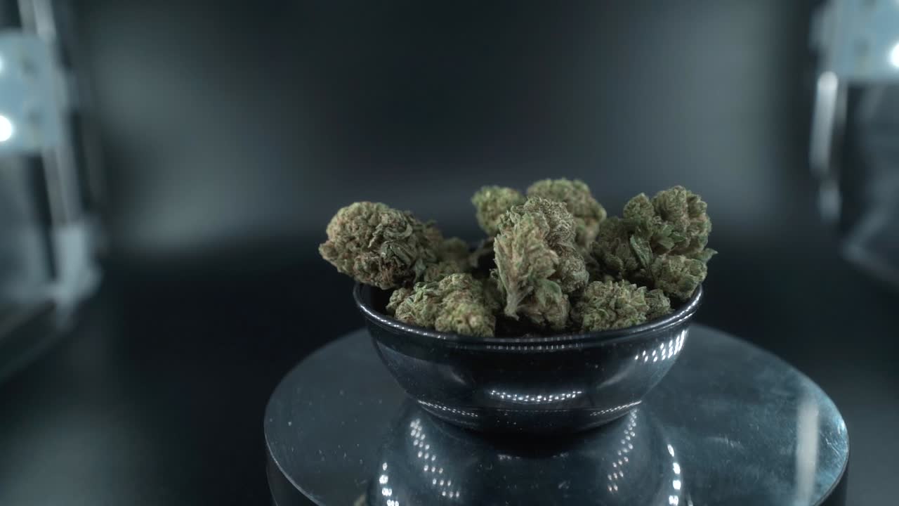 Green Dried Marijuana Buds Close Up Shot, pile of dried marijuana plants in a shiny bowl, trichomes strains, on a reflecting rotating stand, studio lights, cinematic slow motion 120 fps follow right