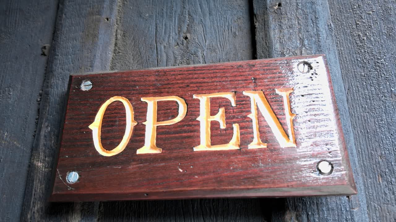 Carved wooden sign on old entrance door reads 'Open' hand held shot