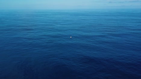 tiro de drone se aproximando de um barco encalhado no meio do mar azul profundo