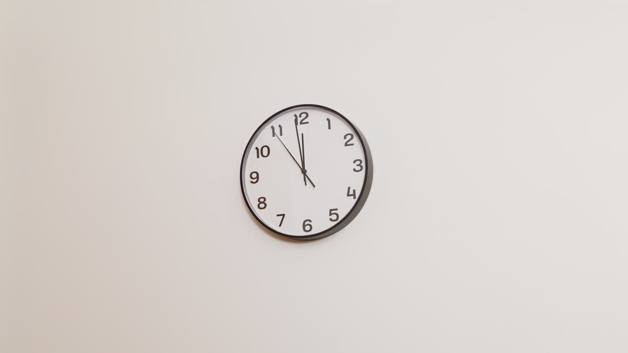 Un orologio da parete da ufficio semplice ma funzionale su una parete bianca neutra, che mostra le 11:59 in uno spazio di lavoro pulito e ordinato