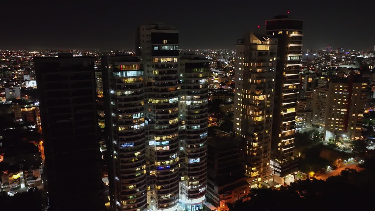 toma en órbita de drones de edificios de torre de lujo iluminados en la avenida anacaona por la noche, santo domingo
