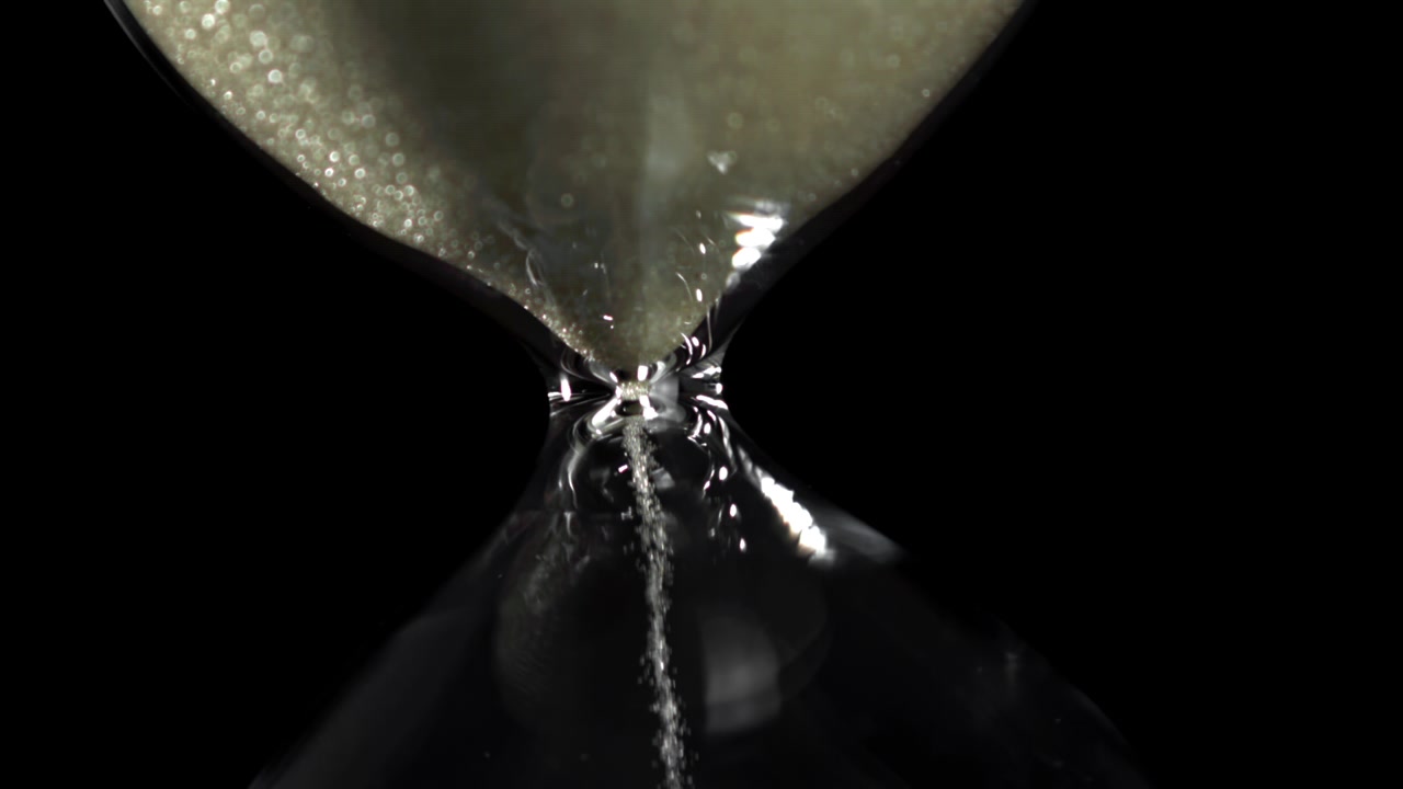 Detailed Close-up of Sand Flowing in an Hourglass Against a Black Background