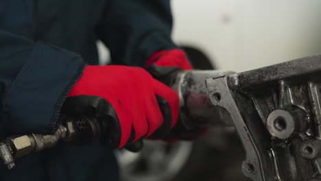 close-up of engineer's hands in red gloves using a pneumatic tool on an engine block in an industrial workshop, mechanical repair, precision craftsmanship, and automotive maintenance in progress