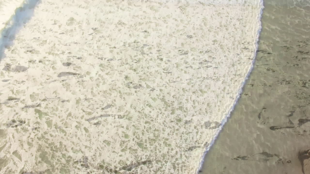Waves washing over sandy beach with footprints and seaweed scattered around