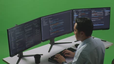 side view of asian man developer using computer to write code with multiple screens in green screen studio