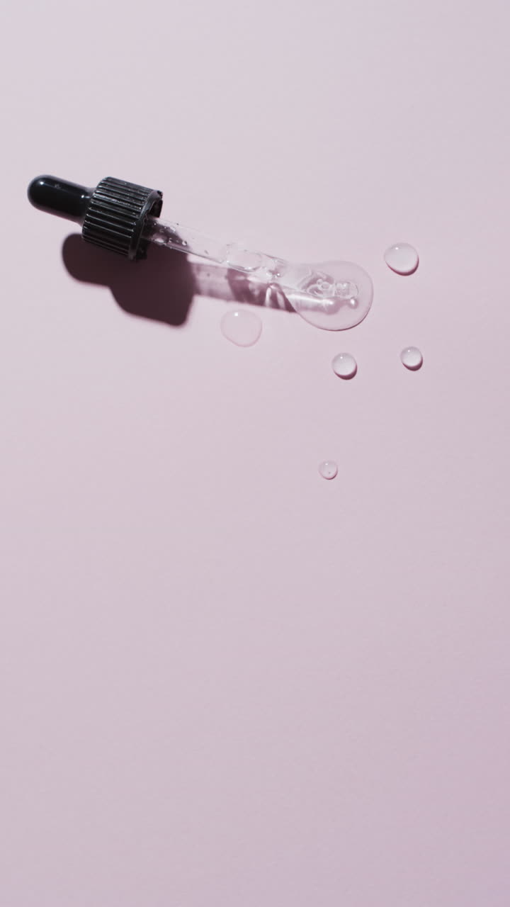 Video verticale di pipetta per trucco e gocce di siero con spazio per il testo su sfondo rosa