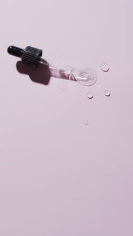 vertical video of make up pipette and drops of serum with copy space on pink background