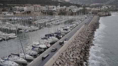 Convoy-of-dark-coloured-vehicles-driving-along-wealthy-marina-harbour-aerial-tracking-shot