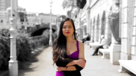 young asian woman walking towards camera, hidden indicated smile, purple dress, black and whtie background