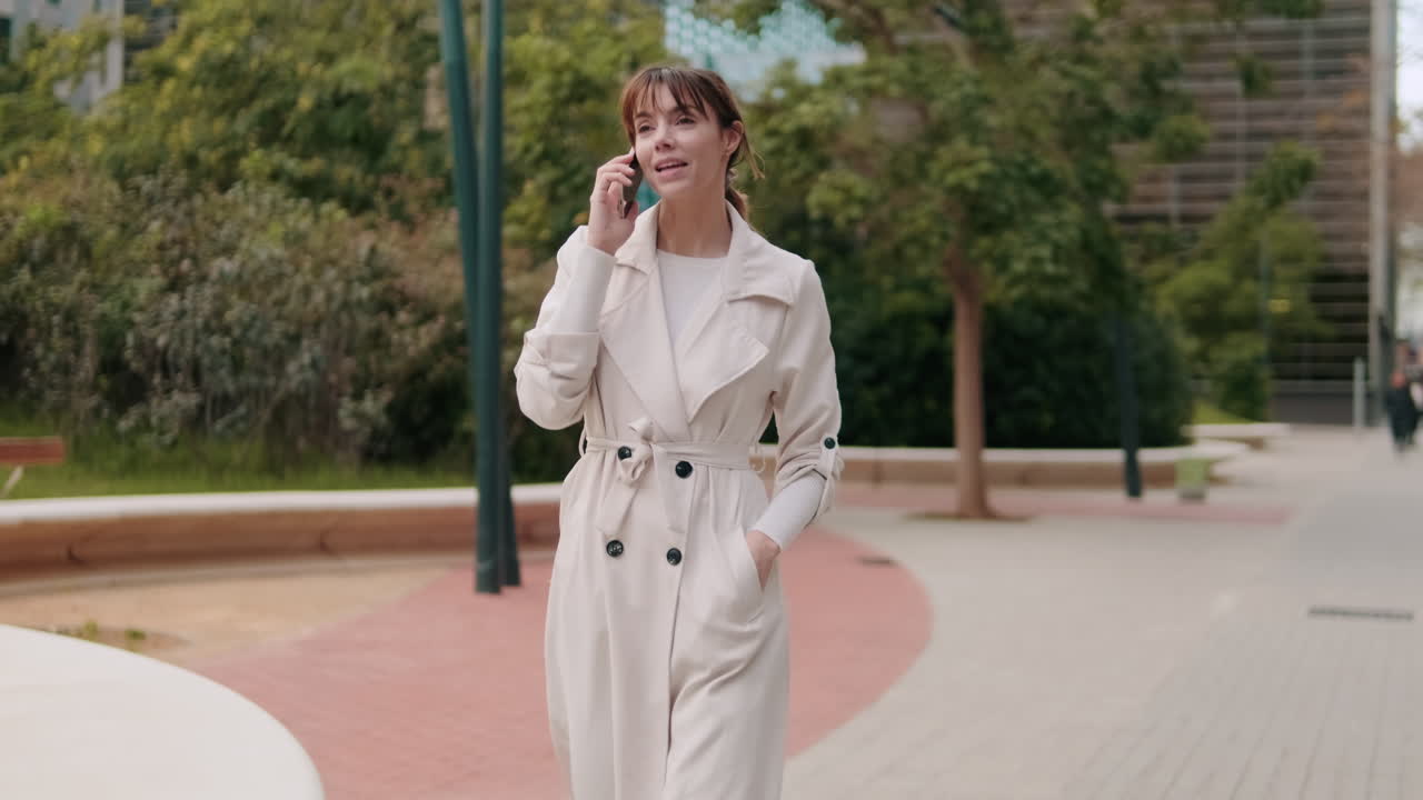 Happy Young Woman Walking and Talking on Smartphone in Park