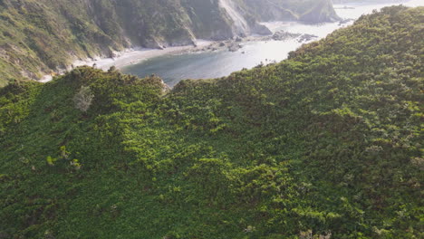 Aerial-View-Of-Beautiful-Wild-Cliff-Coastline-On-A-Sunny-Day-While-People-Are-On-The-Beach