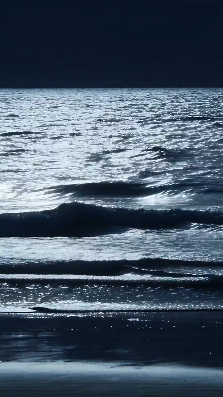Vertical video: Rolling banded surf moon-glinting and cresting toward shore, being pushed by breeze