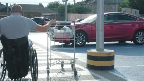 man with disabilities in wheelchair pushing cart in front of himself at supermarket parking