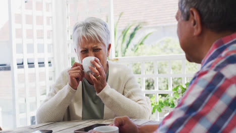 Happy-senior-mixed-race-couple-having-coffee-talking-in-garden