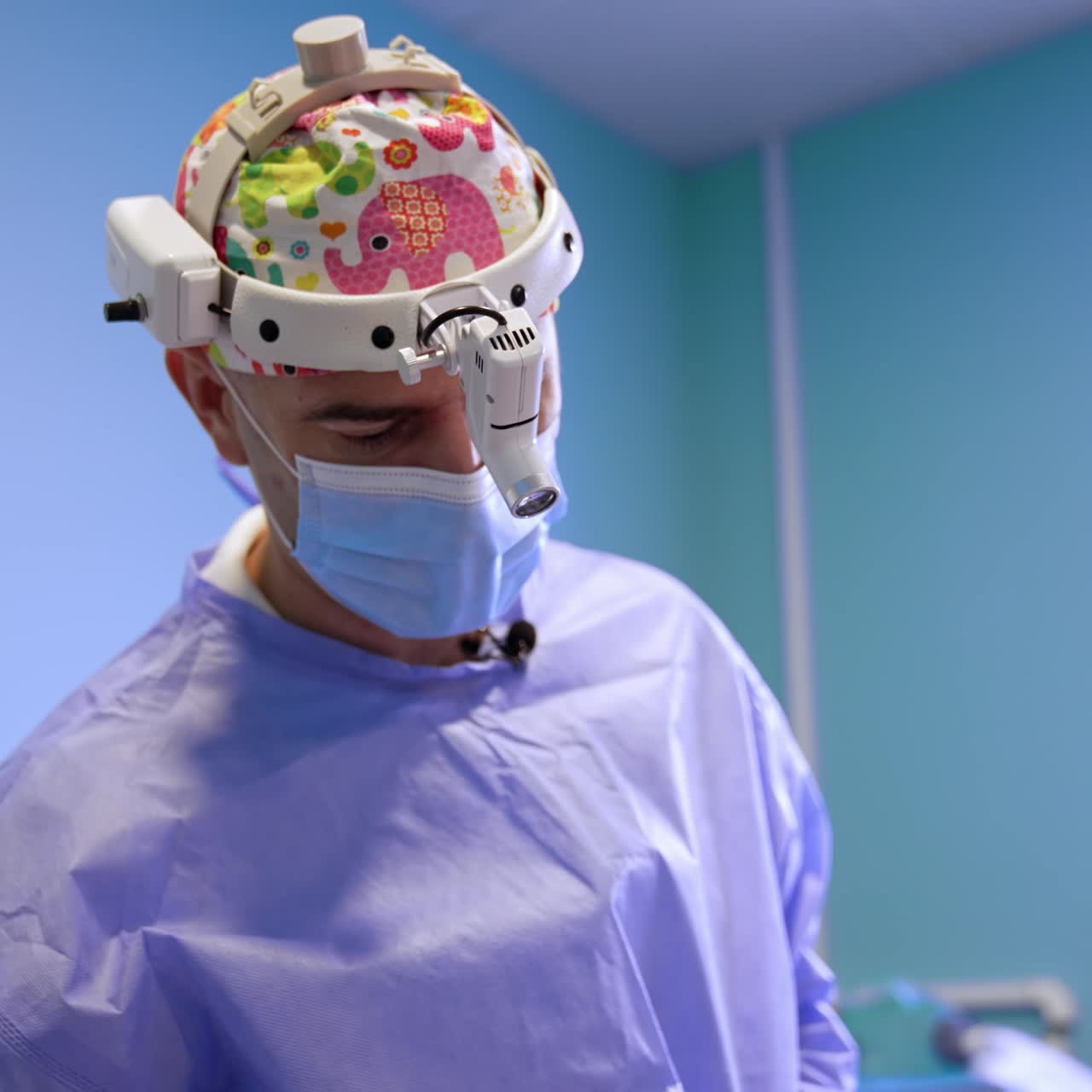 Mid aged Caucasian doctor in mask and headlight covers the operational spot with iodine. The patient is prepared for surgery. Low angle view
