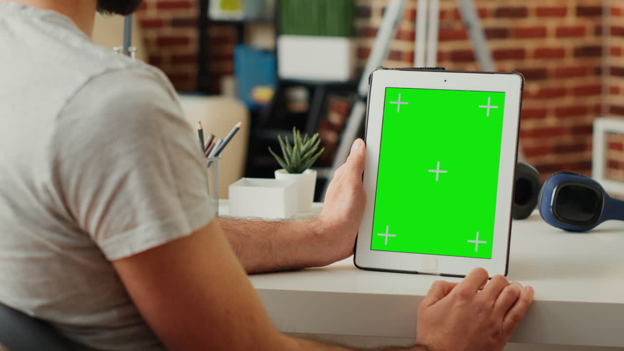 Young man vertically holding digital tablet with greenscreen template
