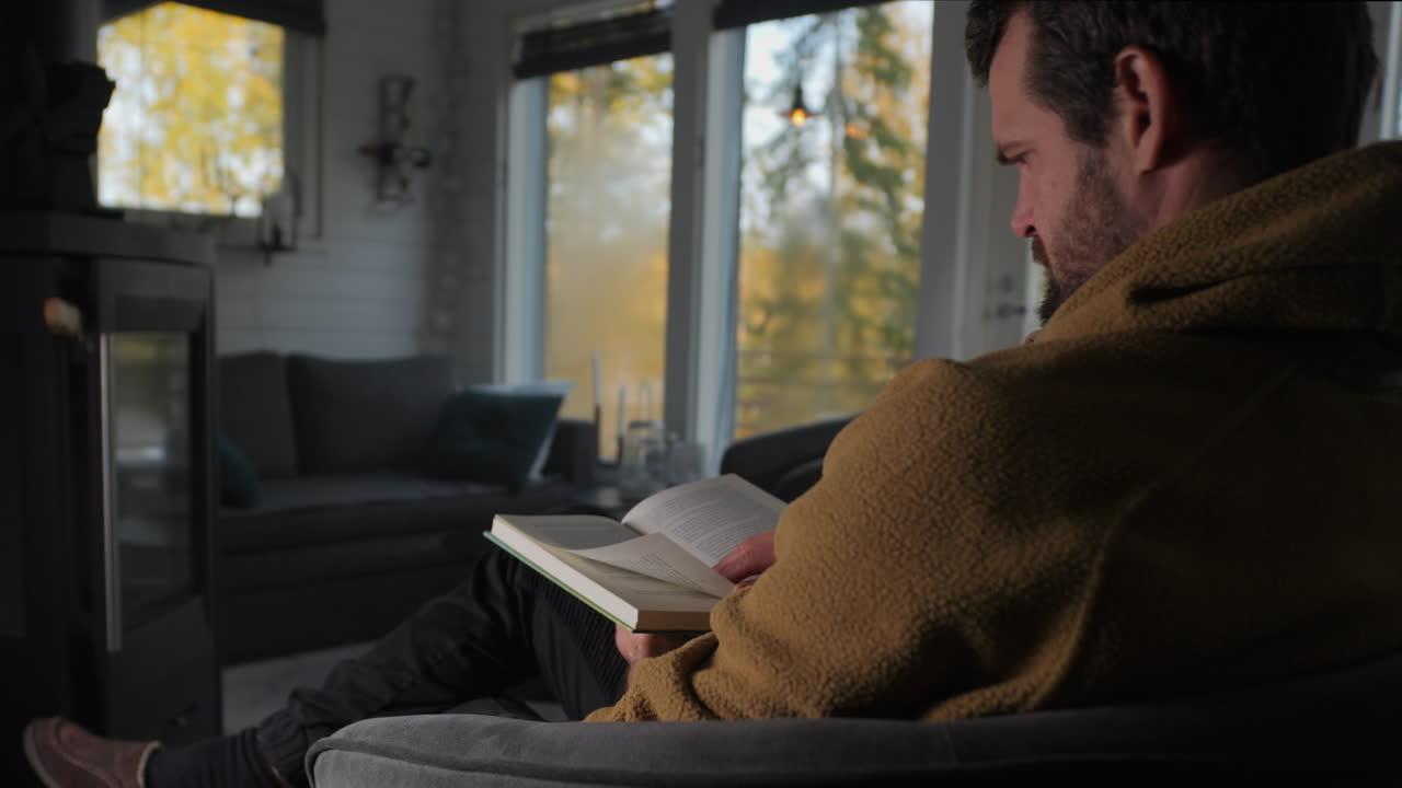 Caucasian man reading a book in a warm cottage in the woods