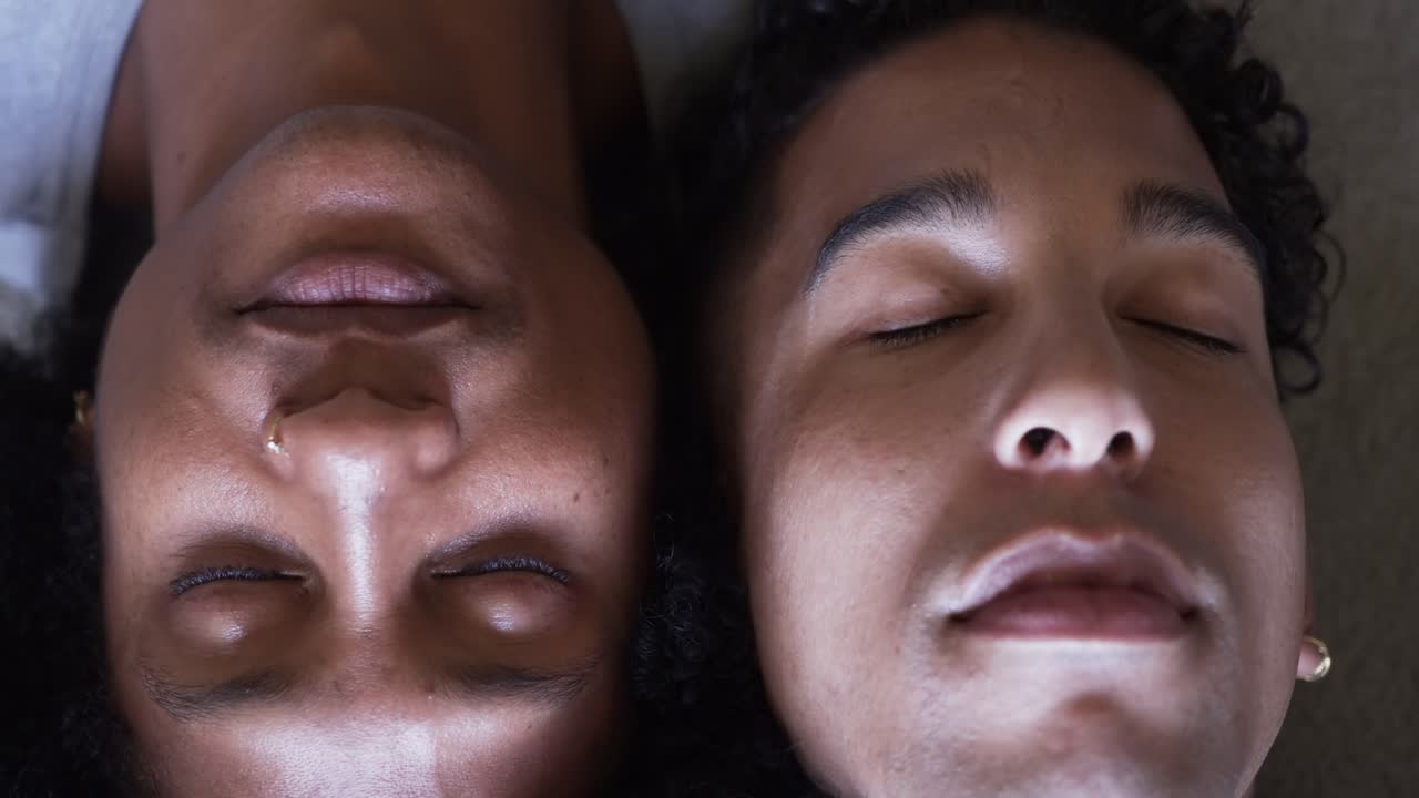 Two African American men lying in bed, left man opening eyes, meeting gaze, smiling, tear, earring