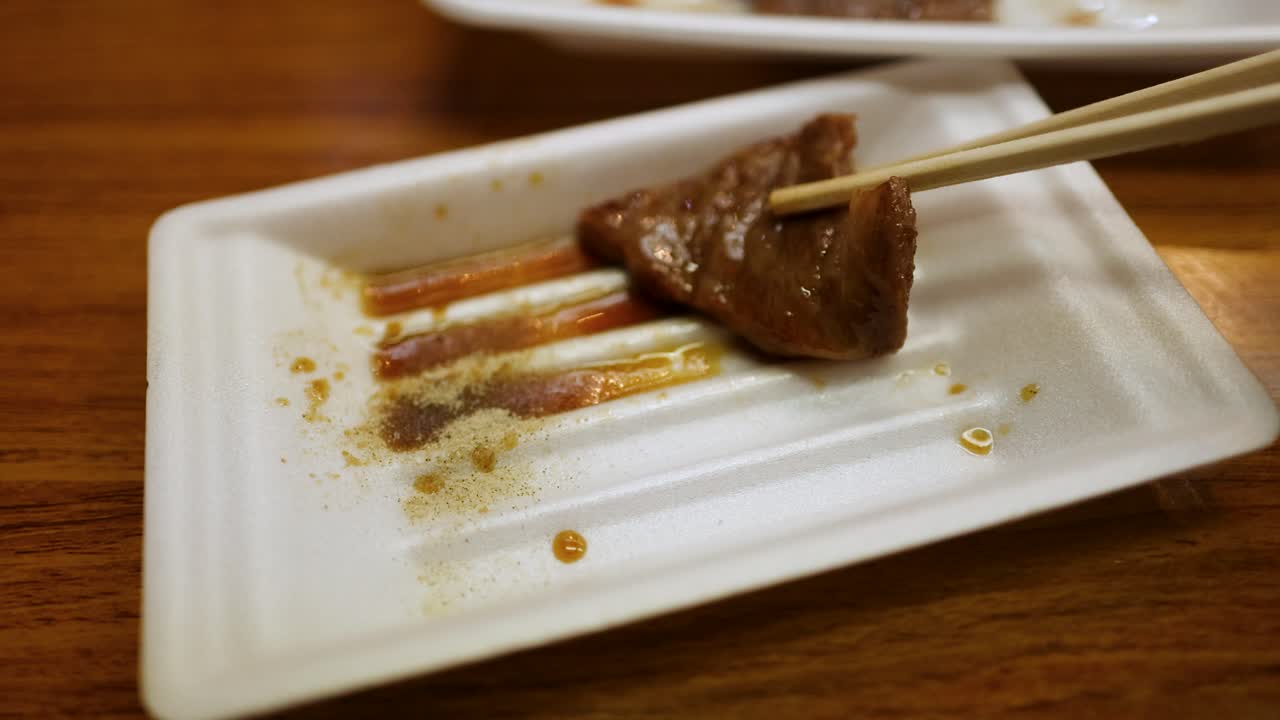 Primo piano di bacchette che intingono un pezzo di manzo alla griglia in salsa e spezie.