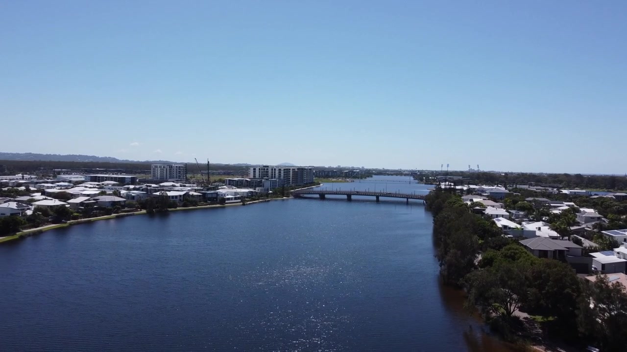 Vista aérea 4K de uma lagoa com uma ponte ao fundo e ladeada por casas particulares à beira-mar na Austrália.