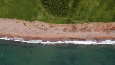 drone shot going to the left following the beautiful contrast of where the massive cliffs meet the beach and the atlantic ocean located on cape breton island in the province of nova scotia, canada