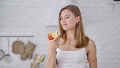 half-length portrait of young woman with apple. beautiful girl is eating a fresh organic fruit in the kitchen. healthy food. dieting concept.