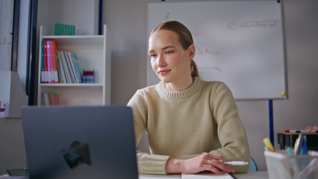 Smiling woman teaching online lesson using laptop sitting at class room closeup