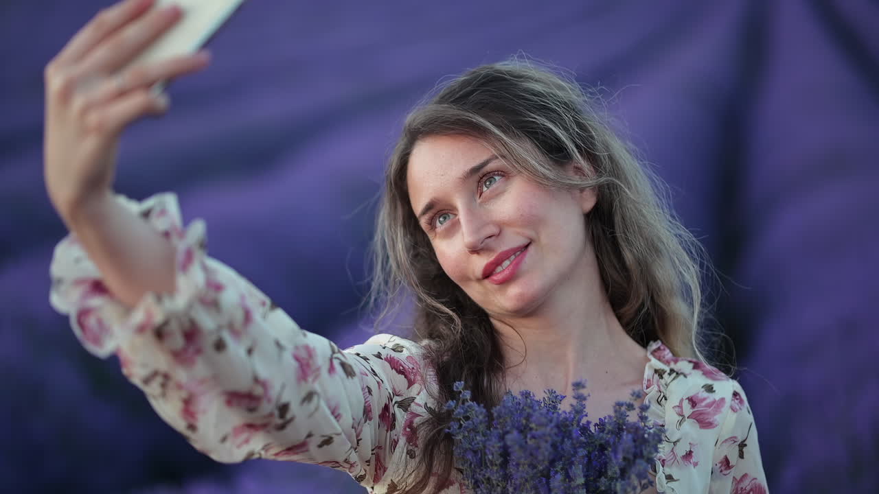 Una giovane donna gioiosa si scatta un selfie mentre tiene in mano un bouquet di lavanda in un campo viola