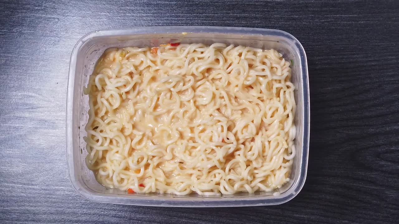 Overhead shot of falling pieces of the sausage in noodles with sauce on wooden table in the kitchen