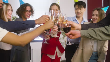 multiethnic colleagues with party hat toasting and drinking at the office party 1