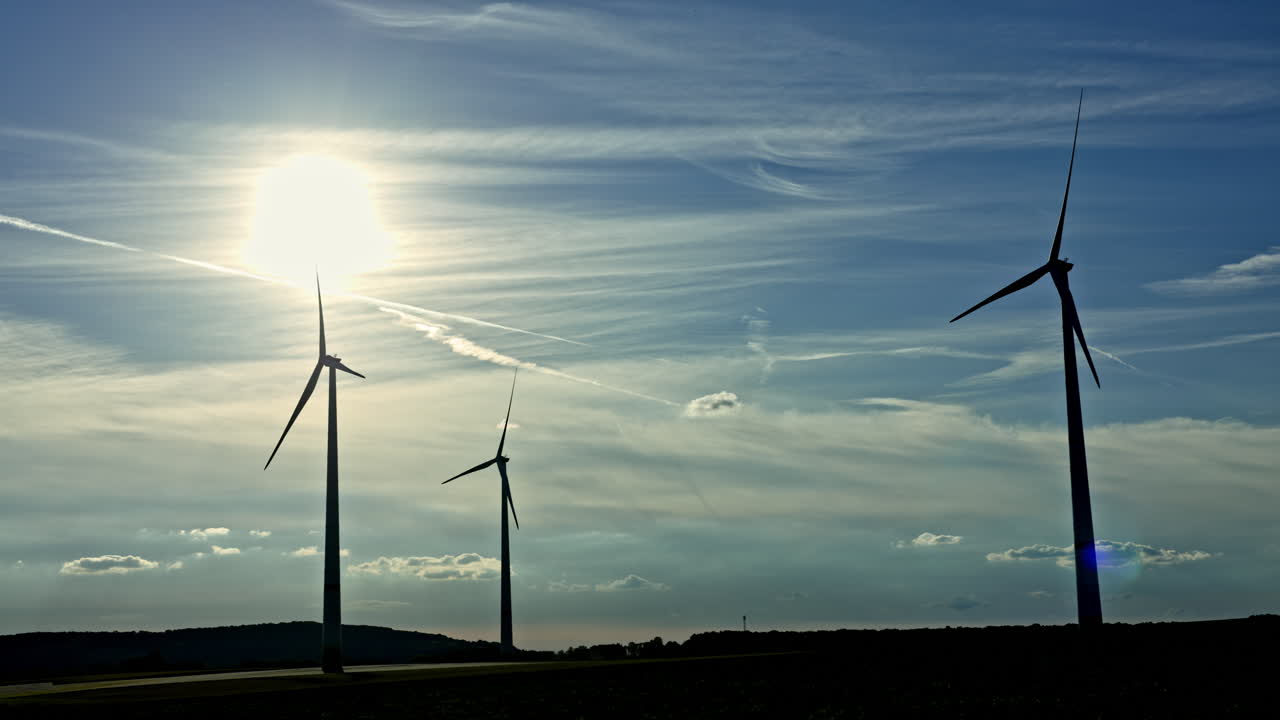 Powerful wind turbines against a cloudy blue sky at sunset. Energy generation by windmills in an endless field. European wind turbine field