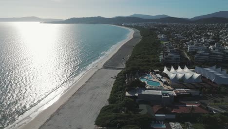 Drone-spinning-over-Jurerê-Internacional-Beach,-capturing-the-pristine-coastal-beauty-and-inviting-shores